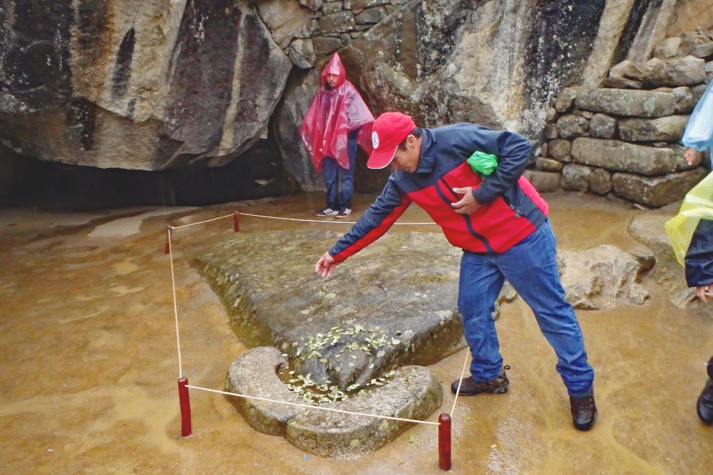 A tour guide at Machu Picchu scatters coca leaves on the condor head platform at the Temple of the Condor. Image Credit: Ed Nellis (c)2013 all rights reserved